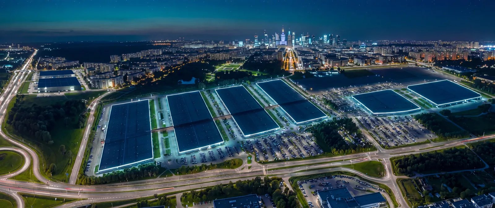 Widok z góry na Ptak Warsaw Expo nocą, w tle panorama Warszawy